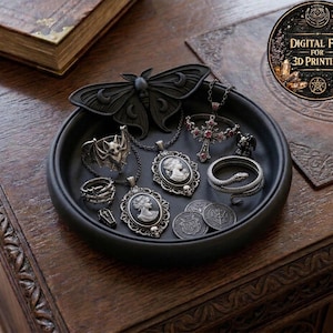 May include: A black tray holds gothic-themed jewelry and accessories, including a moth-shaped ornament, cameo pendants, rings, and a snake ring. The tray also contains coins and a cross pendant. The image includes a digital file for 3D printing.