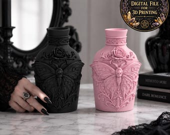 Puede incluir: Dos jarrones decorativos, uno negro mate y otro rosa pastel, cada uno con un diseño en relieve de una polilla con un tórax en forma de calavera, una rosa en el cuello y volutas intrincadas. Los jarrones tienen cuello cilíndrico y cuerpo redondeado.