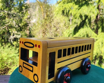 May include: A wooden toy school bus with black wheels and red accents. The bus has a yellow body and black windows. The bus is sitting on a green surface.