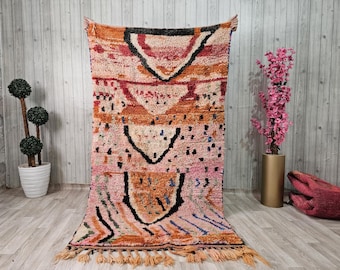Könnte beinhalten: Ein marokkanischer Teppich in Rosa, Orange und Blau mit geometrischem Muster. Der Teppich hat einen Fransenrand und ist aus Wolle.
