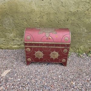 May include: A red decorative chest with a domed lid and brass accents. The chest features intricate patterns and designs, with a rectangular base and curved top. The chest is approximately 24 inches wide and 18 inches tall.