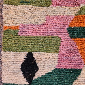 May include: A colorful, textured rug with a geometric pattern. The rug features blocks of pink, green, orange, black, and beige. The rug's design is a mix of geometric shapes and colors, creating a vibrant and eye-catching piece.