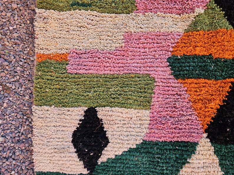 May include: A colorful, textured rug with a geometric pattern. The rug features blocks of pink, green, orange, black, and beige. The rug's design is a mix of geometric shapes and colors, creating a vibrant and eye-catching piece.