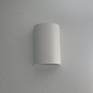 Puede incluir: Un aplique de pared blanco de forma ovalada con una superficie lisa.