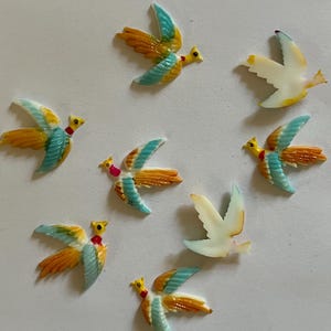 May include: Eight small decorative birds made of painted ceramic. The birds are in various poses with wings spread and are painted in shades of blue, yellow, and white.
