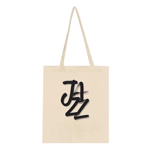 Könnte beinhalten: Eine cremefarbene Tragetasche mit dem Wort "JAZZ" in fetten, schwarzen Pinselstrichen. Die Tasche hat lange, passende Träger zum Über-die-Schulter-Tragen. Das Design ist schlicht und stilvoll, geeignet für Bücher, Lebensmittel oder persönliche Gegenstände.