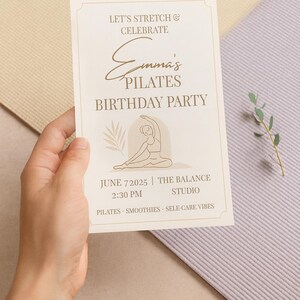 “Printable Pilates Birthday Party invitation held in someone’s hand with pastel yoga mats in the background. Calm, natural lighting and soft tones emphasize the elegant minimalist design. Overlay text reads ‘Editable in Canva – Instant Download’.”