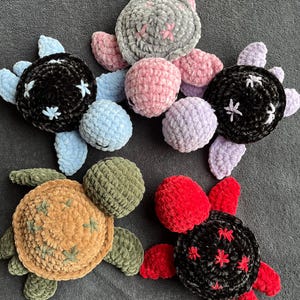 Peut inclure: Cinq jouets en peluche de tortues crochetées dans différentes couleurs, notamment noir, rouge, vert, rose et bleu. Chaque tortue a une carapace détaillée avec un motif d'étoiles.