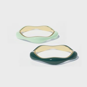 May include: Two resin bangles. One is a light green colour, and the other is a dark green colour. Both have a wavy, organic shape with a gold-coloured interior. The bangles are displayed on a white background.