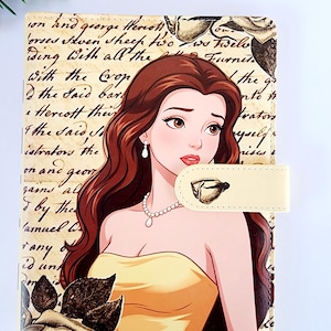 May include: A rectangular notebook cover featuring a printed illustration of a woman with long brown hair wearing a yellow dress and pearl necklace. The background displays vintage-style cursive script text and rose graphics. A cream-colored magnetic strap.
