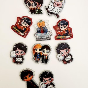 May include: A collection of ten acrylic pins featuring cartoon-style characters with large eyes and glasses, including a boy with a lightning bolt scar, a white owl, and a pumpkin-headed figure at a DJ deck labeled Halloween Music Party.