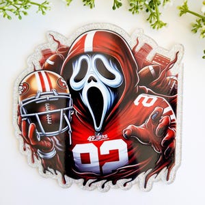 May include: A glittery sticker featuring a character in a red hooded jersey with the number 92 and the text 49ERS. The character holds a gold and red football helmet. The background includes footballs and a stadium silhouette in red tones.
