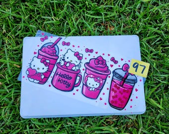 May include: A white rectangular tray featuring four pink Hello Kitty drink illustrations. The drinks include Hello Kitty characters and the words "Hello Kitty". A yellow tag with the number "97" is attached.