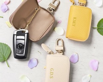 May include: A collection of personalized leather keychains in various colors, including beige and yellow. Each keychain features a zipper closure, a gold-colored clasp, and initials. One keychain is open, displaying a car key. The image also includes the text "CUSTOM DESIGN".