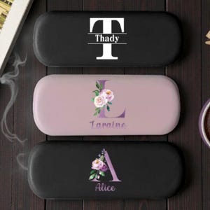 Pode incluir: Três estojos de óculos personalizados. A caixa superior é preta com o nome "Thady" e uma inicial "T" branca. A caixa do meio é roxa clara com o nome "Laraine" e uma inicial "L" floral. A caixa inferior é preta com o nome "Alice" e uma inicial "A" floral.