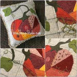 May include: A close-up of a handmade felt pumpkin pillow with a brown stem and green leaves. The pillow is made of various shades of orange, red, and brown felt and is decorated with beads around the edge. The pillow is on a brown surface. The text "Three Sheep Studio.com" is embroidered on the pillow.