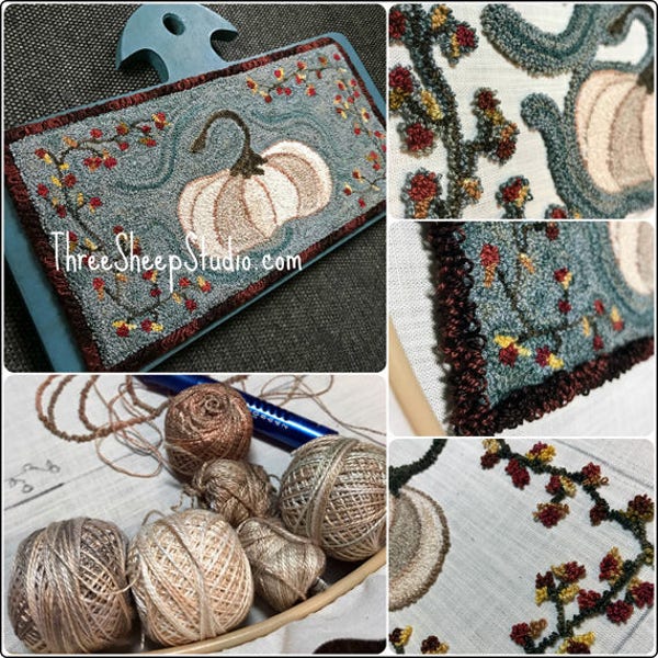 May include: A handmade rug with a pumpkin design, set on a blue wooden base. The rug features a light blue background with a pumpkin and fall foliage. The text "ThreeSheepStudio.com" is visible. Various spools of yarn are also shown.