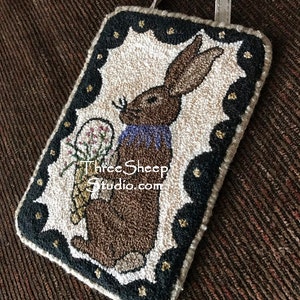 May include: A brown bunny with a purple collar holds a bouquet of pink flowers in its paws. The bunny is surrounded by a black and gold frame with a scalloped edge. The image includes the text "Three Sheep Studio.com".