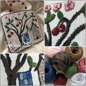 May include: A close-up of a needlepoint craft project depicting a house with a tree and cherries. The project is framed with a brown wooden frame and has a brown handle. The project is surrounded by various colored yarn balls.