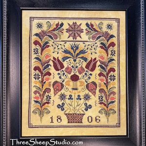May include: Framed cross-stitch sampler with a floral design in shades of red, blue, yellow, and green. The sampler features a central floral arrangement, flanked by symmetrical floral borders. The year 1806 is stitched at the bottom. The frame is black.
