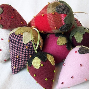 May include: A collection of nine felt strawberry ornaments, each with a different fabric pattern and color. The strawberries are decorated with small beads and have a rustic, handmade look.