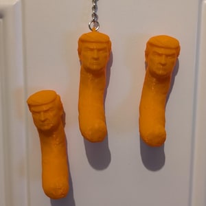 May include: Three orange-colored novelty keychains shaped like a popular snack food, each with a sculpted face. The keychains are hanging from a silver keyring against a white door.