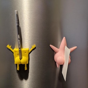May include: Yellow and pink 3D printed character magnets. The yellow character is holding a silver pen. The pink character is holding a white note.