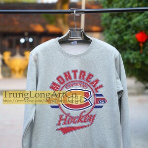 Puede incluir: Una sudadera gris con un logotipo de hockey de los Canadiens de Montreal de estilo vintage. El logotipo presenta el nombre del equipo, "Canadiens", y el n&uacute;mero "09" en rojo, blanco y azul. El texto "Hockey" est&aacute; impreso debajo del logotipo en una fuente roja, blanca y azul.