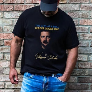 Może przedstawiać: Czarny t-shirt z fotografią Wołodymyra Zełenskiego i tekstem "This is what a real leader looks like".