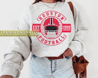 Könnte beinhalten: Hellgraues Sweatshirt mit rotem und schwarzem Footballhelm-Grafik und den Worten "HOUSTON FOOTBALL EST 1999". Das Sweatshirt hat einen Rundhalsausschnitt und lange Ärmel.