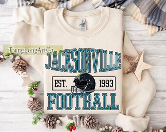 May include: Cream-colored sweatshirt featuring the text "JACKSONVILLE FOOTBALL" in teal and black, with a football helmet graphic and the year "1993". The design is centered on the front of the garment.