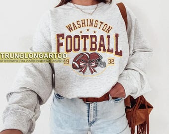 May include: A light gray sweatshirt with the words "WASHINGTON FOOTBALL" in maroon and gold lettering. The design includes a football, helmet, and bow. The number "32" is also visible.