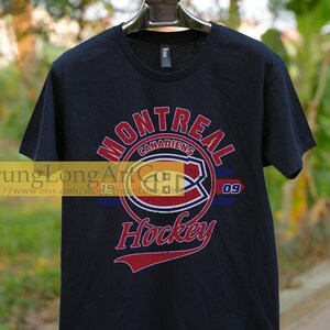 Puede incluir: Camiseta negra con un gr&aacute;fico de estilo vintage del logotipo del equipo de hockey de los Canadiens de Montreal. El logotipo presenta una "C" roja, blanca y azul dentro de un c&iacute;rculo con las palabras "Canadiens de Montreal" y "Hockey" en letras rojas. El n&uacute;mero "09" est&aacute; impreso a la derecha del logotipo.