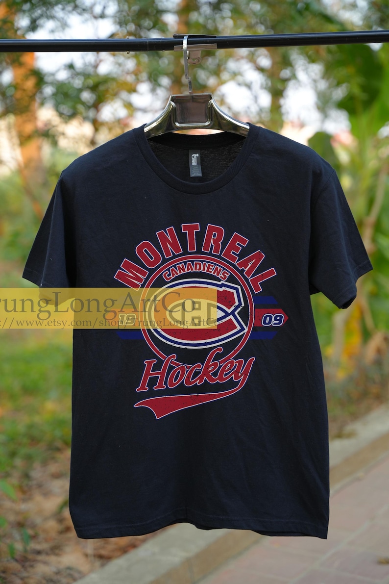 Puede incluir: Camiseta negra con un gr&aacute;fico de estilo vintage del logotipo del equipo de hockey de los Canadiens de Montreal. El logotipo presenta una "C" roja, blanca y azul dentro de un c&iacute;rculo con las palabras "Canadiens de Montreal" y "Hockey" en letras rojas. El n&uacute;mero "09" est&aacute; impreso a la derecha del logotipo.