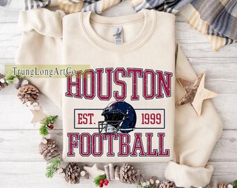 Könnte beinhalten: Cremefarbenes Sweatshirt mit dem Text "HOUSTON FOOTBALL" in Burgunderrot mit Used-Effekt. Eine dunkelblaue Footballhelm-Grafik ist unter dem Wort "HOUSTON" zentriert. Das Jahr "1999" ist unter dem Helm aufgedruckt.