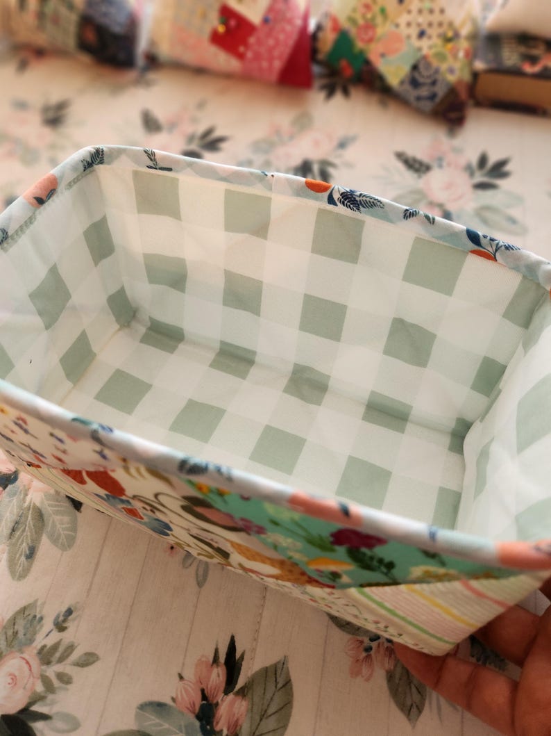Pode incluir: Uma cesta retangular de tecido com um padr&atilde;o floral e xadrez. O interior apresenta um design xadrez verde claro e branco. O exterior tem um padr&atilde;o floral colorido com toques de azul, rosa e laranja. A cesta &eacute; provavelmente feita &agrave; m&atilde;o e adequada para armazenamento.