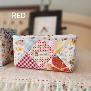 Pode incluir: Uma pequena cesta de tecido feita &agrave; m&atilde;o com um design de patchwork. A cesta apresenta uma variedade de tecidos florais e estampados em vermelho, branco e cores pastel. A palavra "RED" est&aacute; impressa no canto superior esquerdo.