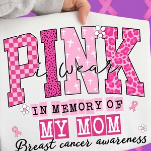 K&ouml;nnte beinhalten: Wei&szlig;es T-Shirt mit den Worten "PINK I wear IN MEMORY OF MY MOM Breast cancer awareness" in Rosa und Schwarz. Das Wort "PINK" hat ein kariertes, Leopardenmuster und Kreuzmuster. Eine Hand h&auml;lt das T-Shirt.