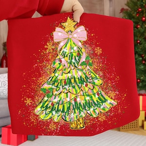 May include: A red Christmas-themed pillow with a colorful, whimsical Christmas tree design. The tree features a gold star, pink bow, and candy cane accents. The background has a speckled effect with gold snowflakes.