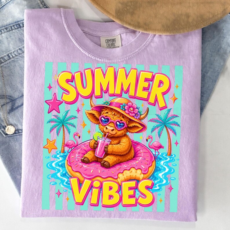 May include: A light purple t-shirt with a colorful graphic. The graphic features a cartoon cow wearing sunglasses and a hat, floating on a donut in water, with the words "SUMMER VIBES".