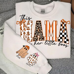 May include: White sweatshirt with the text "This MAMA loves her little boos." The word "MAMA" is in orange and leopard print. The sleeves feature ghost graphics with names. A Halloween-themed apparel item.