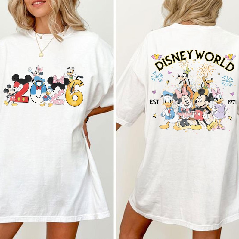 Może przedstawiać: Biała koszulka z postaciami Disneya i napisem "2026" z przodu. Tył koszulki przedstawia "Disney World" z r&oacute;żnymi postaciami i rokiem "1971". Projekt zawiera Myszkę Miki, Minnie, Kaczora Donalda i Goofy'ego.