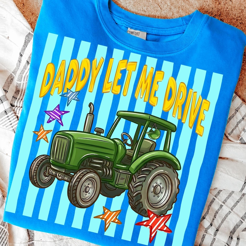 Pu&ograve; includere: Felpa blu con grafica di un trattore verde e la scritta gialla "DADDY LET ME DRIVE". Il design include strisce blu e bianche e stelle colorate.