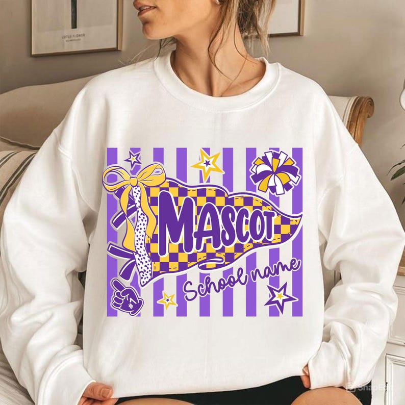 May include: A white long-sleeve sweatshirt featuring a graphic print of a purple and yellow checkered pennant flag with the text MASCOT and School name, accented by a yellow bow, a pom-pom, stars, and a foam finger on a purple striped background.
