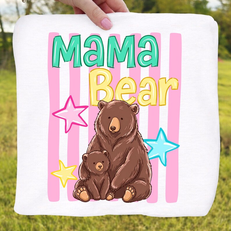 Pu&ograve; includere: Coperta quadrata bianca con le parole "Mama Bear" in verde acqua e giallo, con un'illustrazione di orso bruno e cucciolo. Sfondo a righe rosa e bianche con accenti di stelle. Un design carino e accogliente.