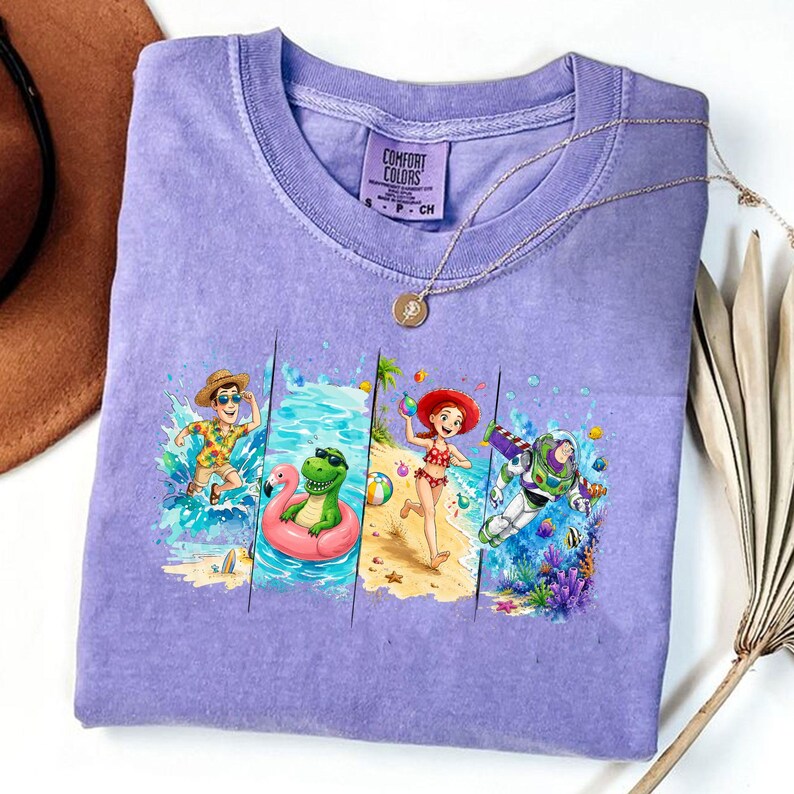May include: A purple Comfort Colors t-shirt featuring a colorful beach scene with cartoon characters. The design includes a man in a Hawaiian shirt, a dinosaur in a flamingo float, a woman in a bikini, and Buzz Lightyear. A gold necklace is draped across the shirt.