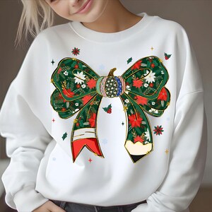 May include: White sweatshirt featuring a large bow design with a pumpkin center. The bow is decorated with red poinsettias, white flowers, and green leaves. The pumpkin has a patchwork design with American flag accents. Festive apparel.