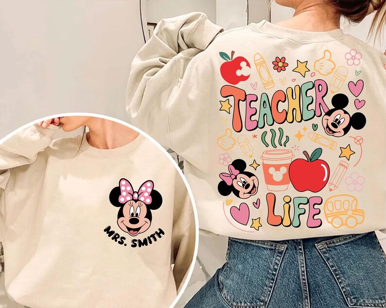 May include: Cream-coloured sweatshirt with a Minnie Mouse graphic and the text "Mrs. Smith" on the front. The back features colourful graphics with the words "Teacher Life" and images of apples, pencils, and Mickey Mouse.