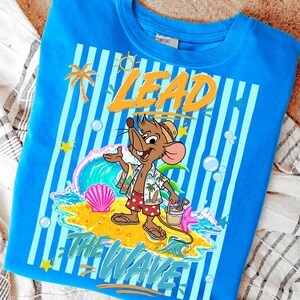 May include: A blue sweatshirt with a cartoon mouse in beach attire, the words "LEAD THE WAVE" are printed on the front. The design includes a wave, palm tree, and seashells. The shirt has a crew neck and a tag that says "COMFORT".
