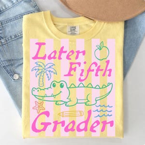 May include: Yellow t-shirt with a pink and white striped design. The shirt features the text "Later Fifth Grader" with a cartoon alligator, palm tree, apple, pencil, starfish, and waves graphic.